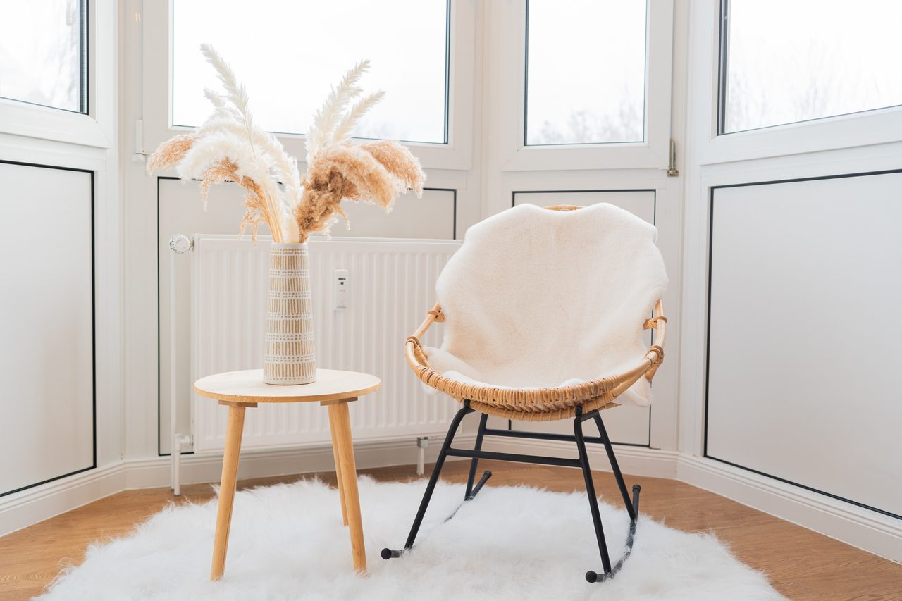 Rattansessel mit Fell, Beistelltisch mit Pampasgras und Teppich am Fenster