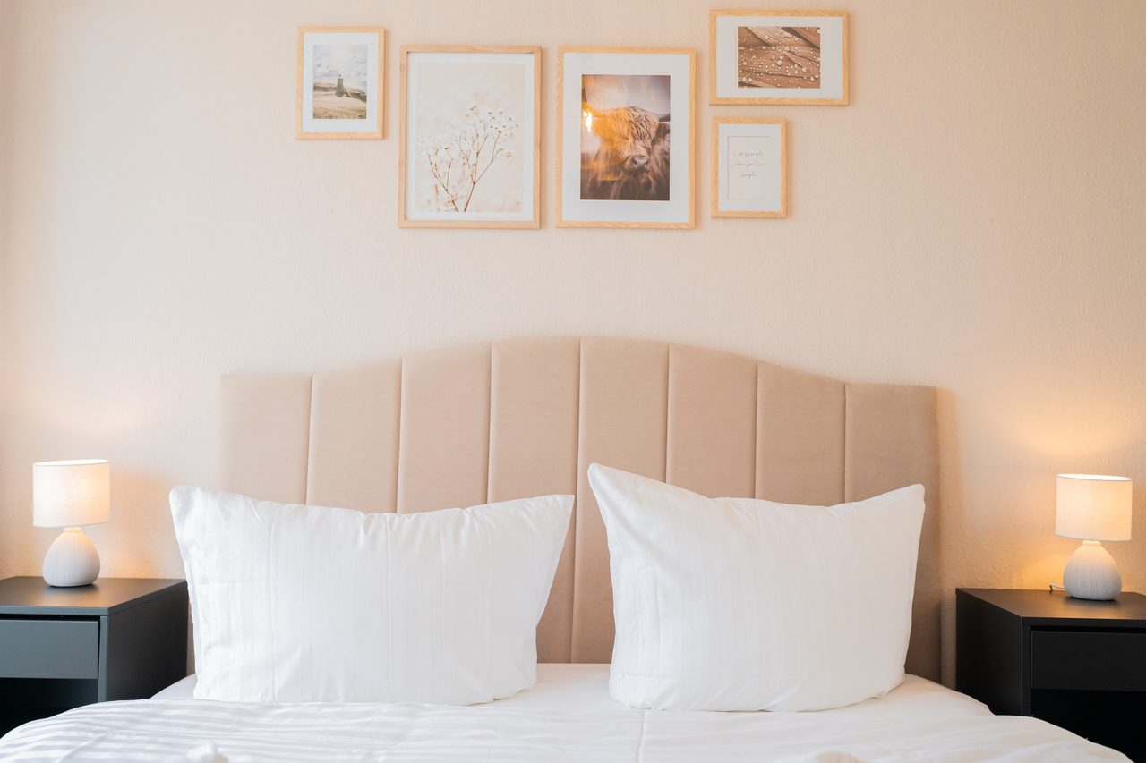 Schlafzimmer mit Doppelbett, Polsterkopfteil, Nachttischlampen und Wandbildern