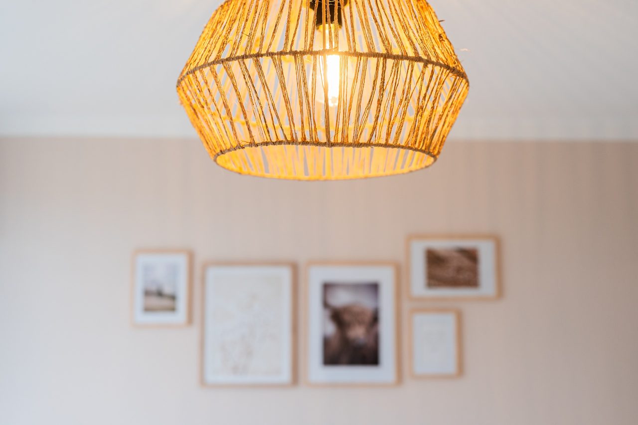 Pendelleuchte aus Rattan vor Bilderrahmen an der Wand