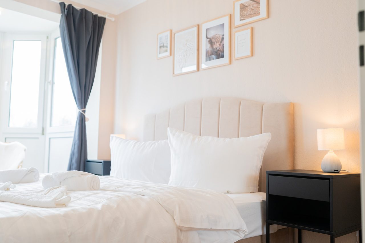 Schlafzimmer mit Doppelbett, schwarzem Nachttisch und Bildern an der Wand