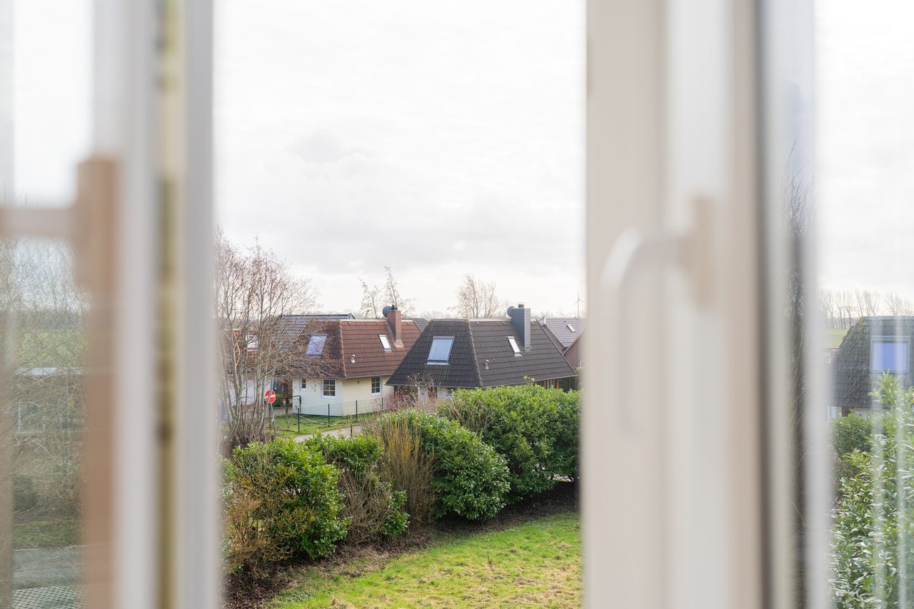 Blick aus dem Fenster auf Hecke, Rasen und Häuser