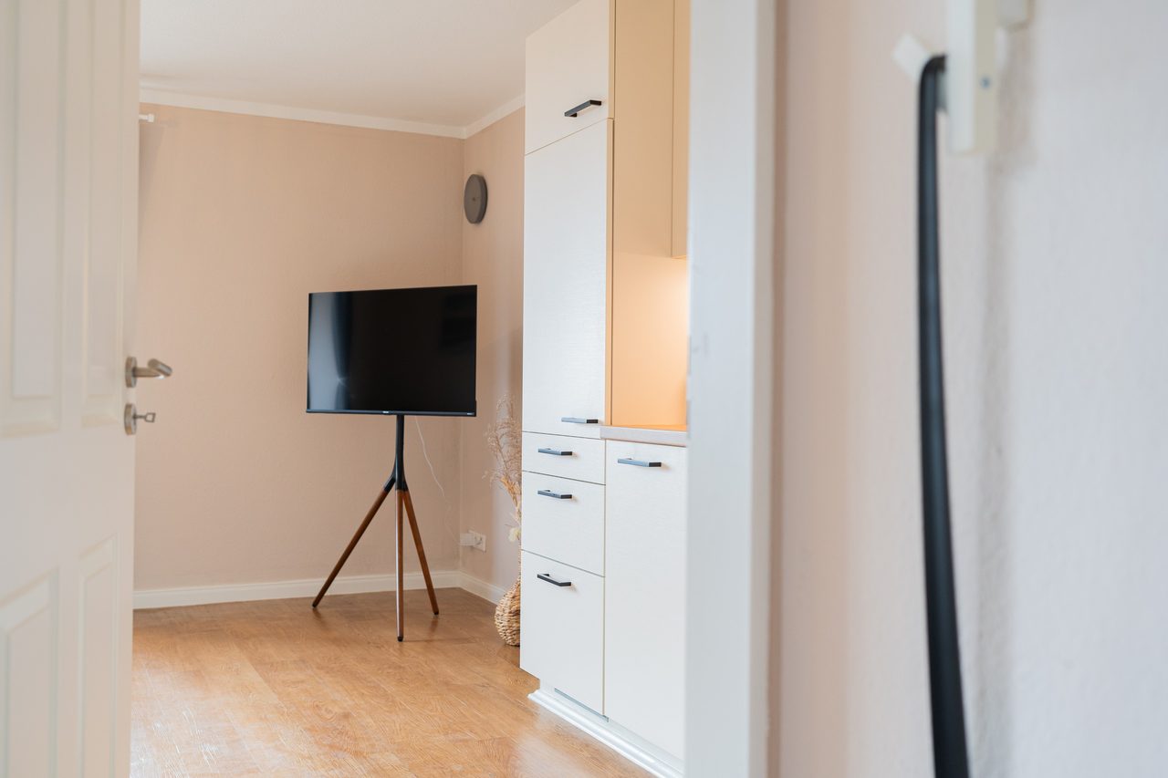 Wohnbereich mit Fernseher auf Ständer, Blick durch eine offene Tür