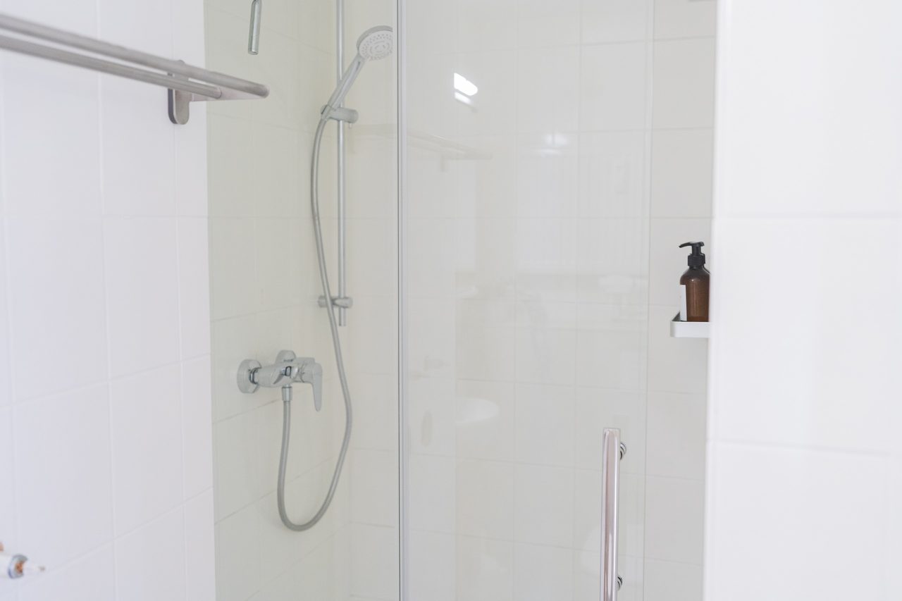 Dusche mit Glastür, Handbrause und weißen Fliesen