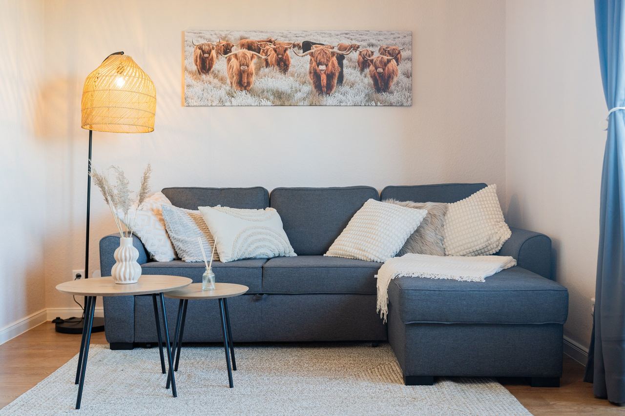 Wohnzimmer mit grauem Ecksofa, Beistelltischen und Stehlampe