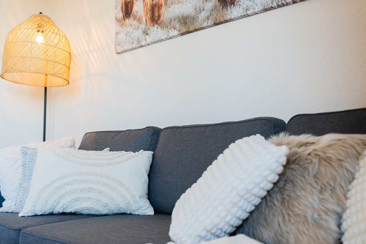 Graues Sofa mit weißen Kissen, Fellkissen und Rattanlampe