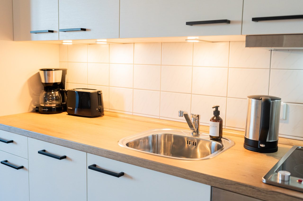 Küche mit Edelstahlspüle, Kaffeemaschine und Wasserkocher auf Holzplatte