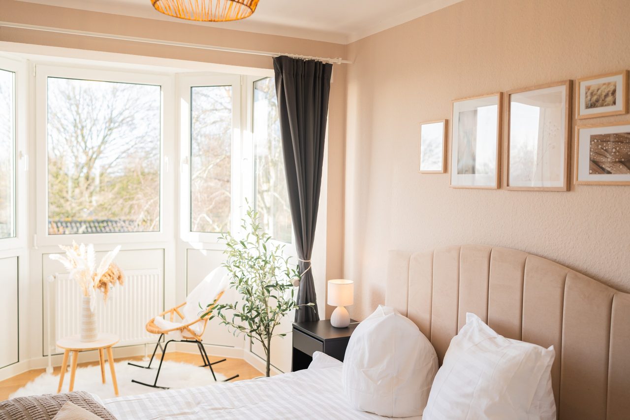 Schlafzimmer mit Doppelbett, Bilderwand und Rattansessel im Erker