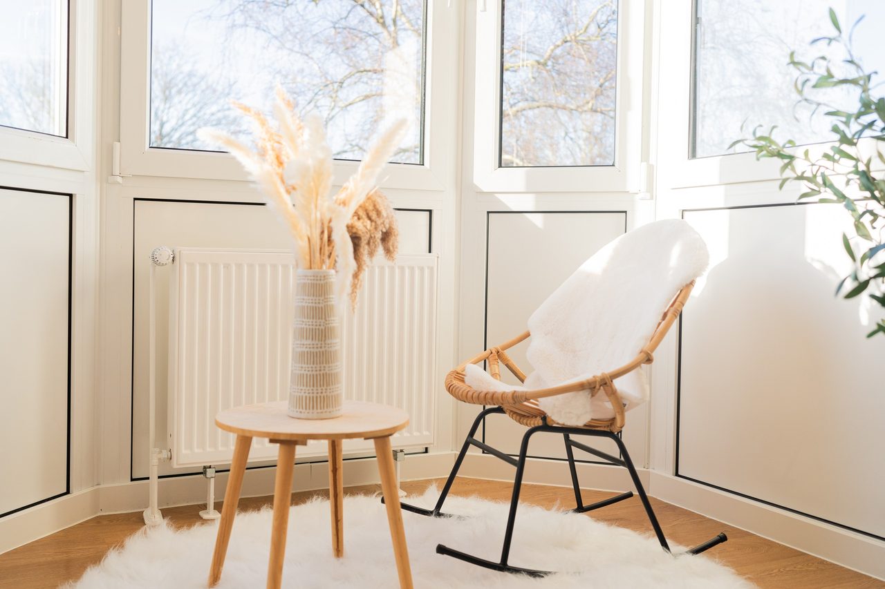 Erker mit Rattan-Schaukelstuhl, Beistelltisch und Trockengras in Vase