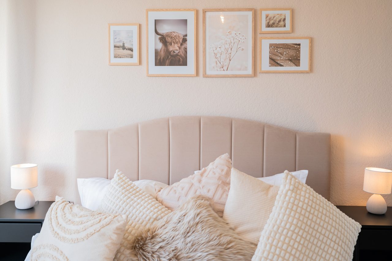 Doppelbett mit vielen Kissen, Fellkissen und Bildern darüber