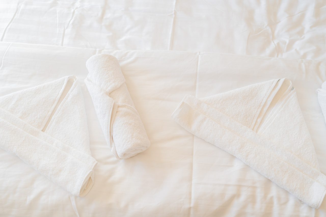 Bett mit weißer Bettwäsche und zwei gerollten Handtüchern
