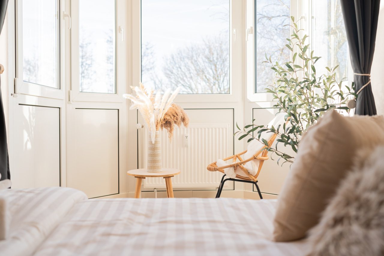 Blick vom Bett auf den Erker mit Rattansessel und Trockengras