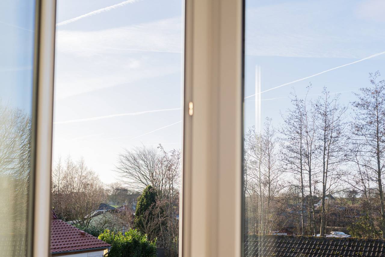 Blick aus dem Fenster auf Bäume und Dächer bei blauem Himmel