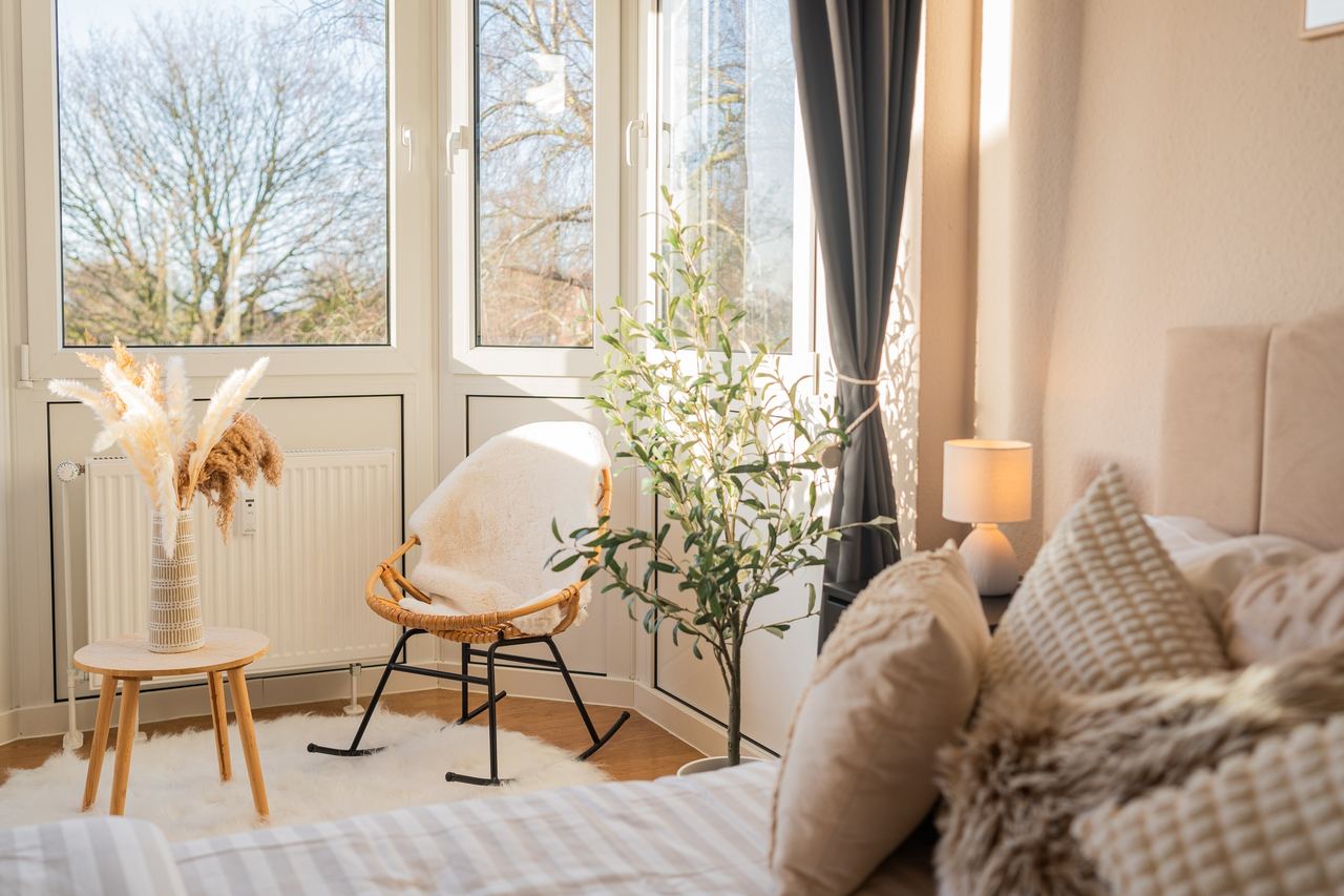 Erker mit Schaukelstuhl, Olivenbäumchen und Bett im Vordergrund