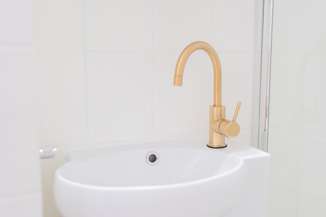 Waschbecken mit goldener Armatur vor weißen Fliesen
