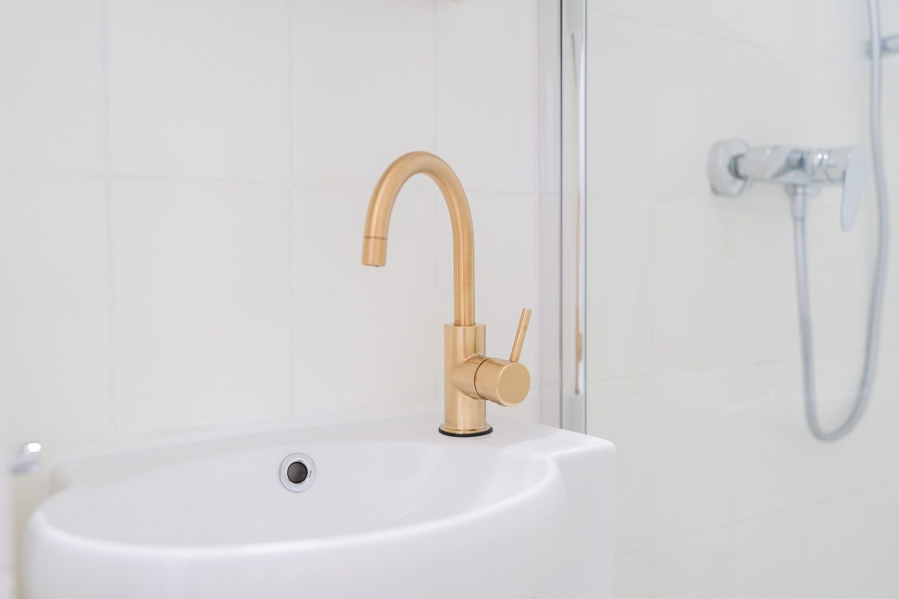 Waschbecken mit goldener Armatur neben der Dusche