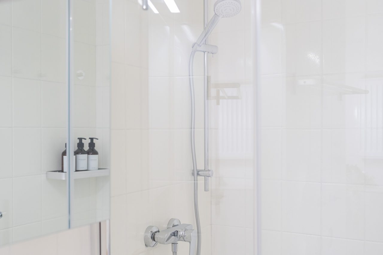 Dusche mit Glaswand, Handbrause und Ablage mit Pflegeprodukten