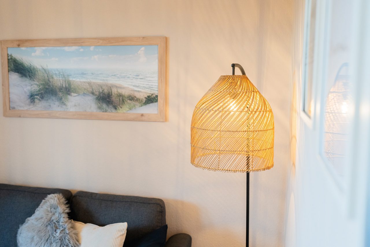 Stehlampe aus Rattan neben Sofa, darüber ein Dünenbild