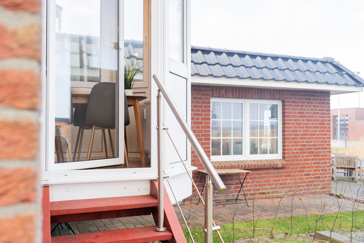 Offene Terrassentür mit Treppe, Blick auf ein Backsteinhaus