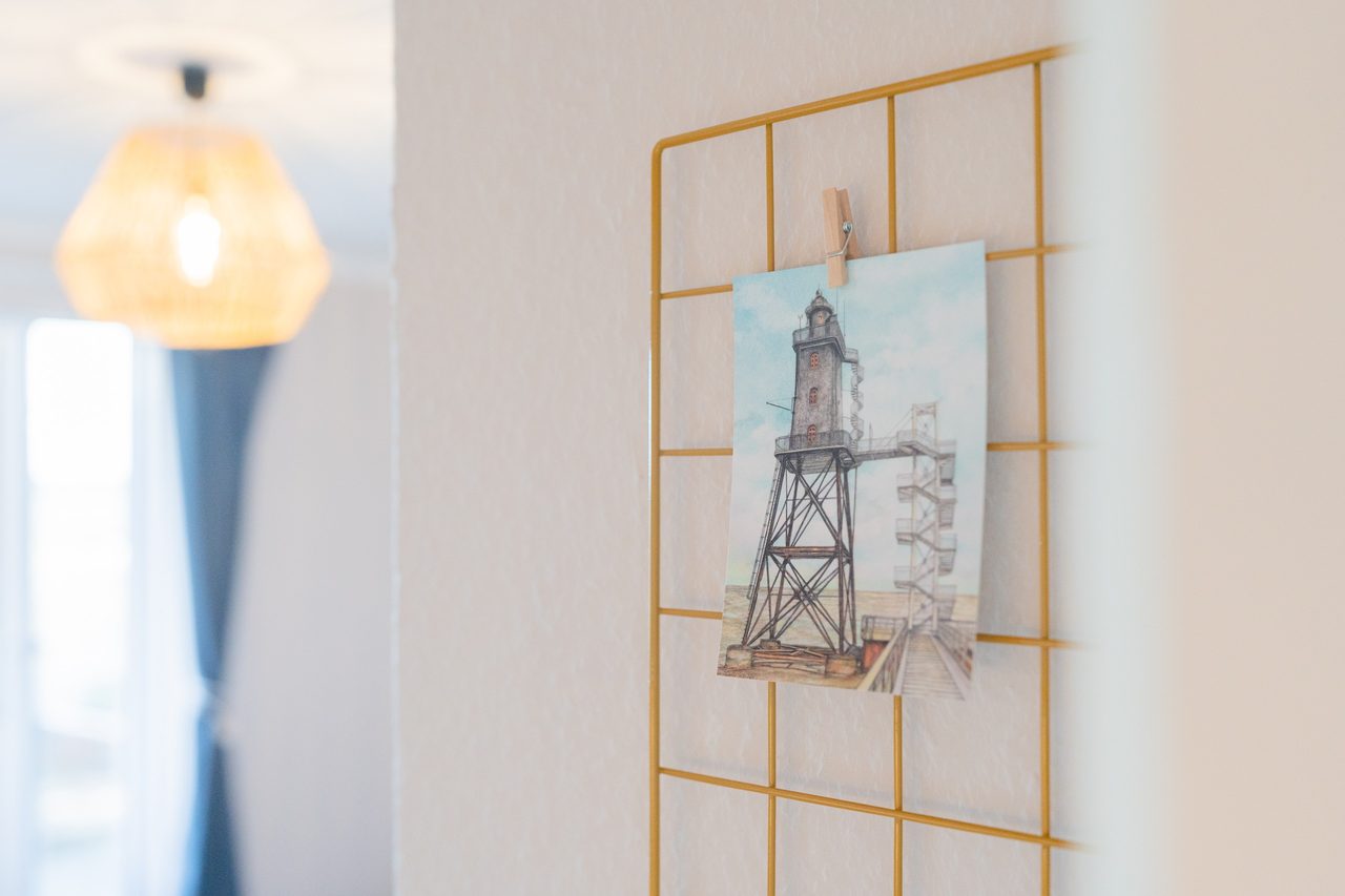 Gitterwand mit Postkarte eines Leuchtturms und Pendelleuchte