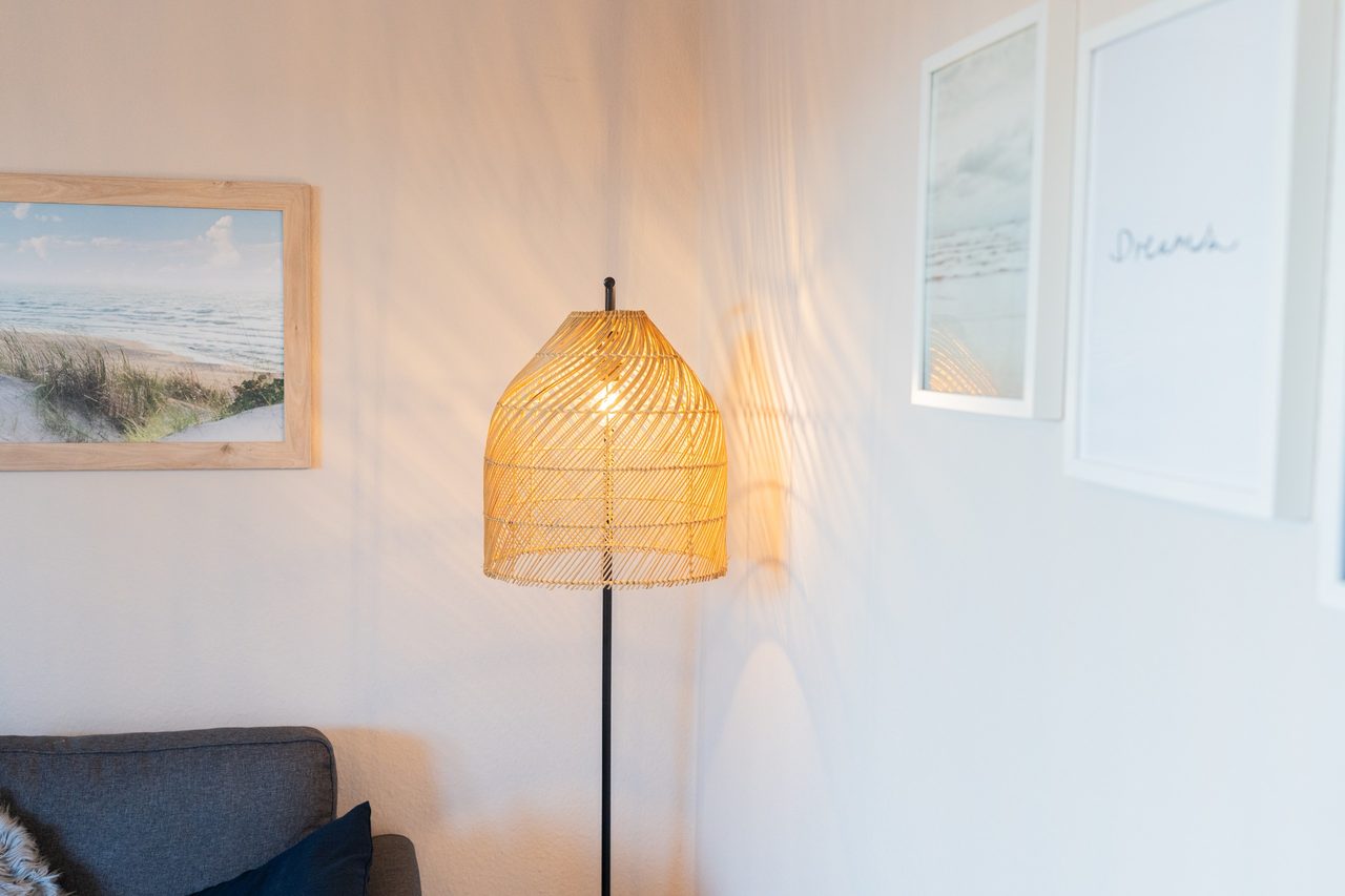 Stehlampe aus Rattan, Dünenbild und Sofa im Wohnbereich