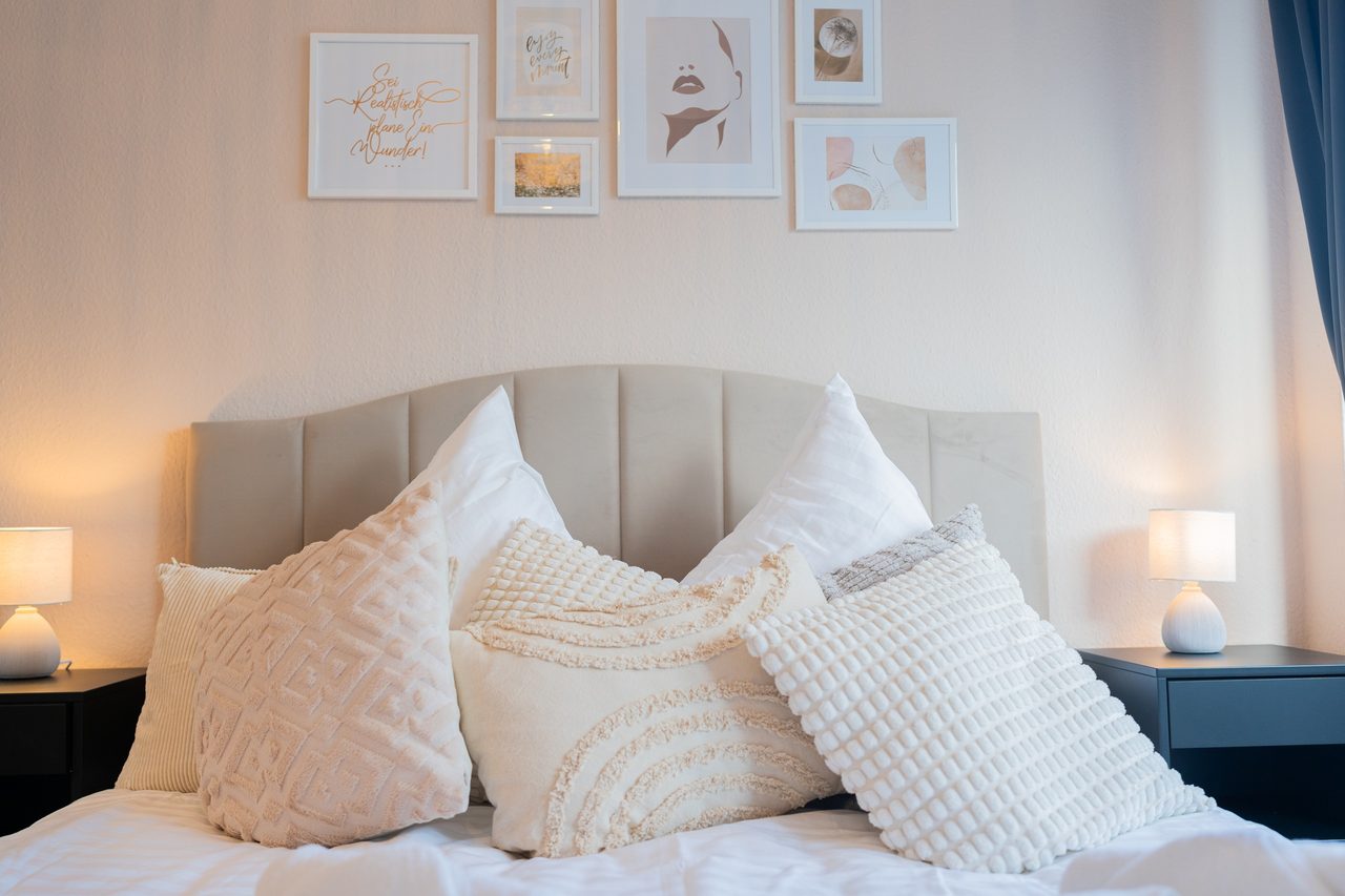 Doppelbett mit Polsterkopfteil, weißen Kissen und Bildern an der Wand
