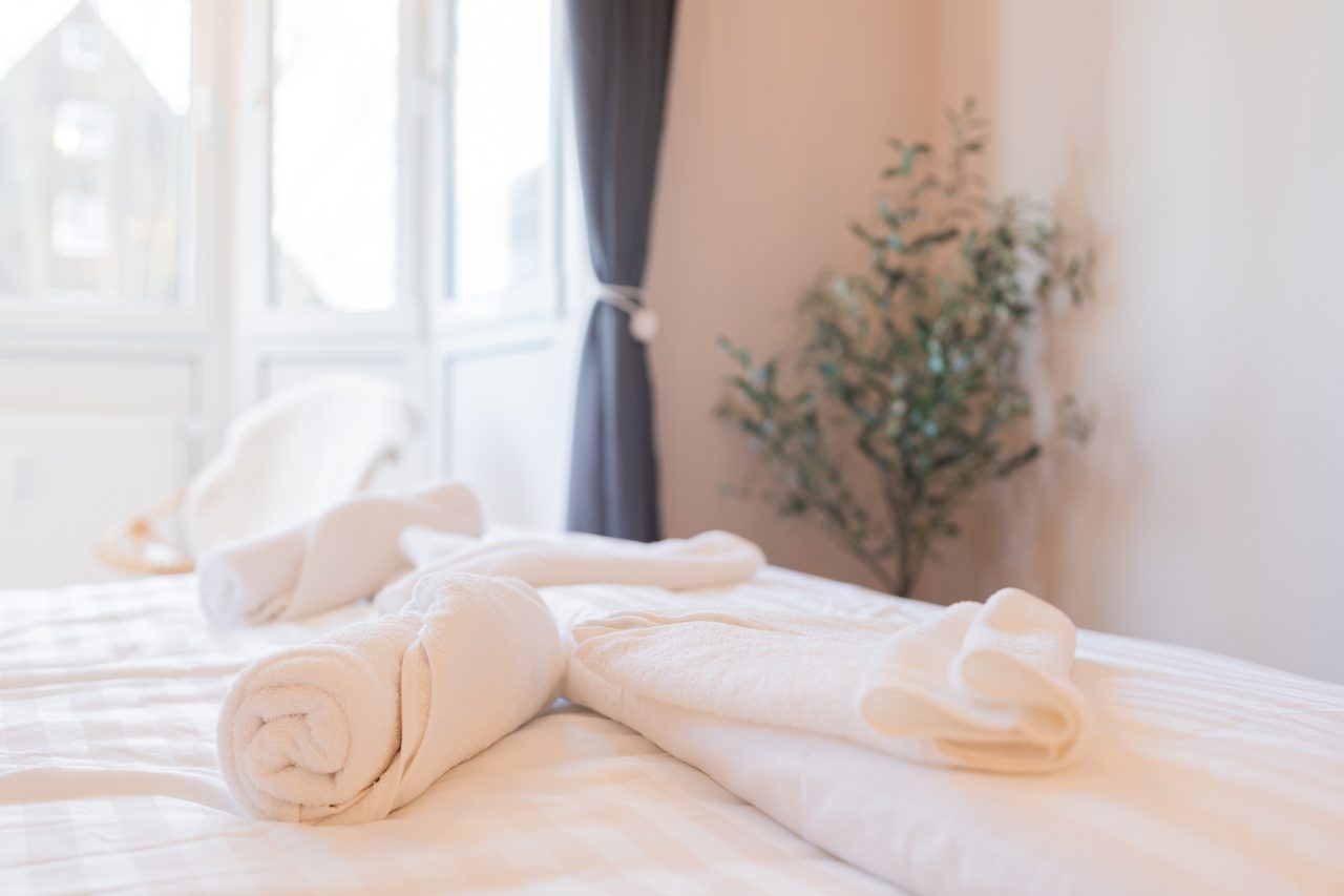 Bett mit gerollten Handtüchern vor einer Fenstertür und Zimmerpflanze