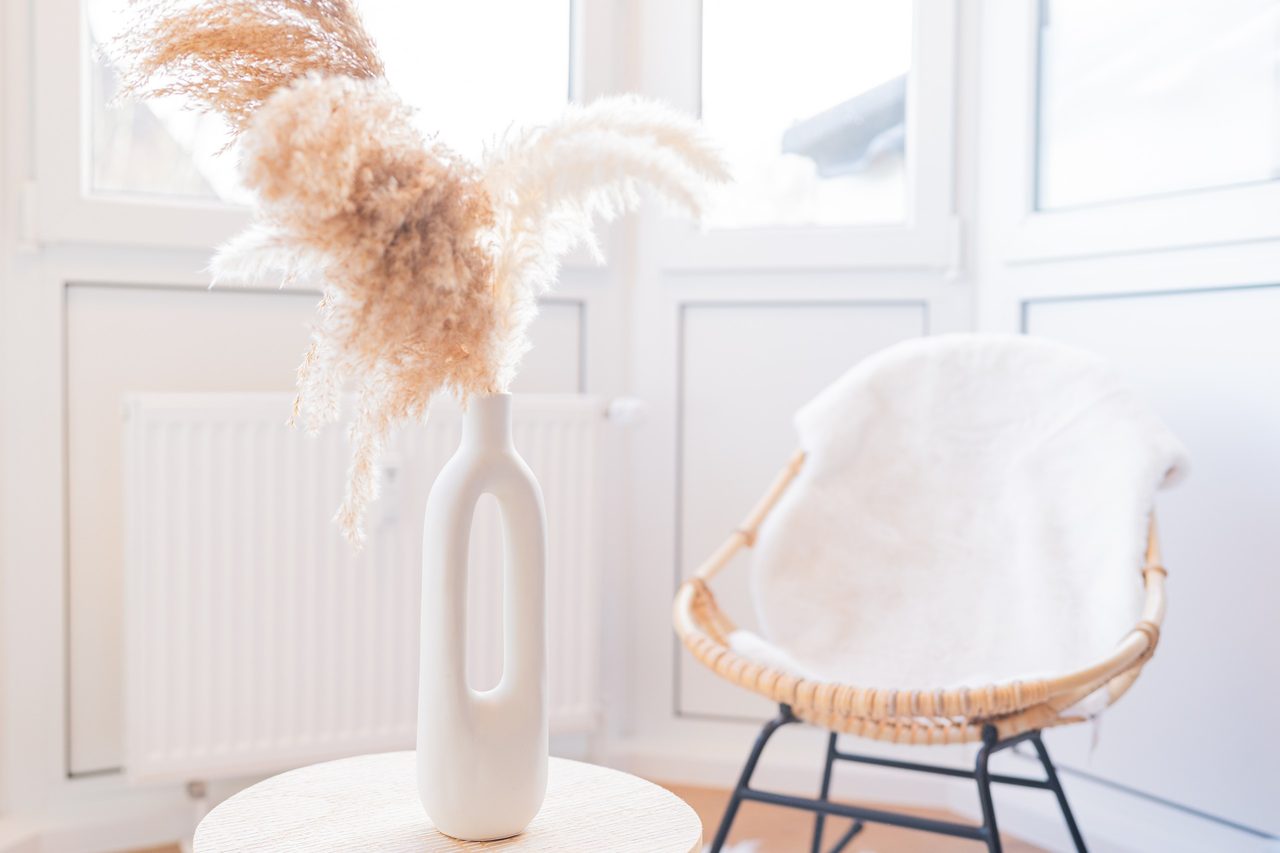 Rattansessel mit Fell und Vase mit Pampasgras vor Fenstern