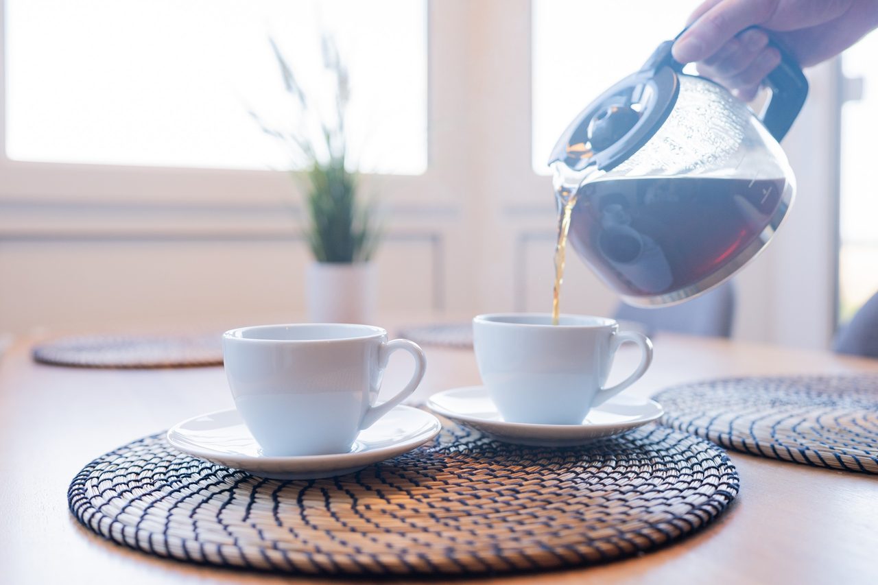 Kaffee wird in zwei weiße Tassen auf einem Esstisch gegossen