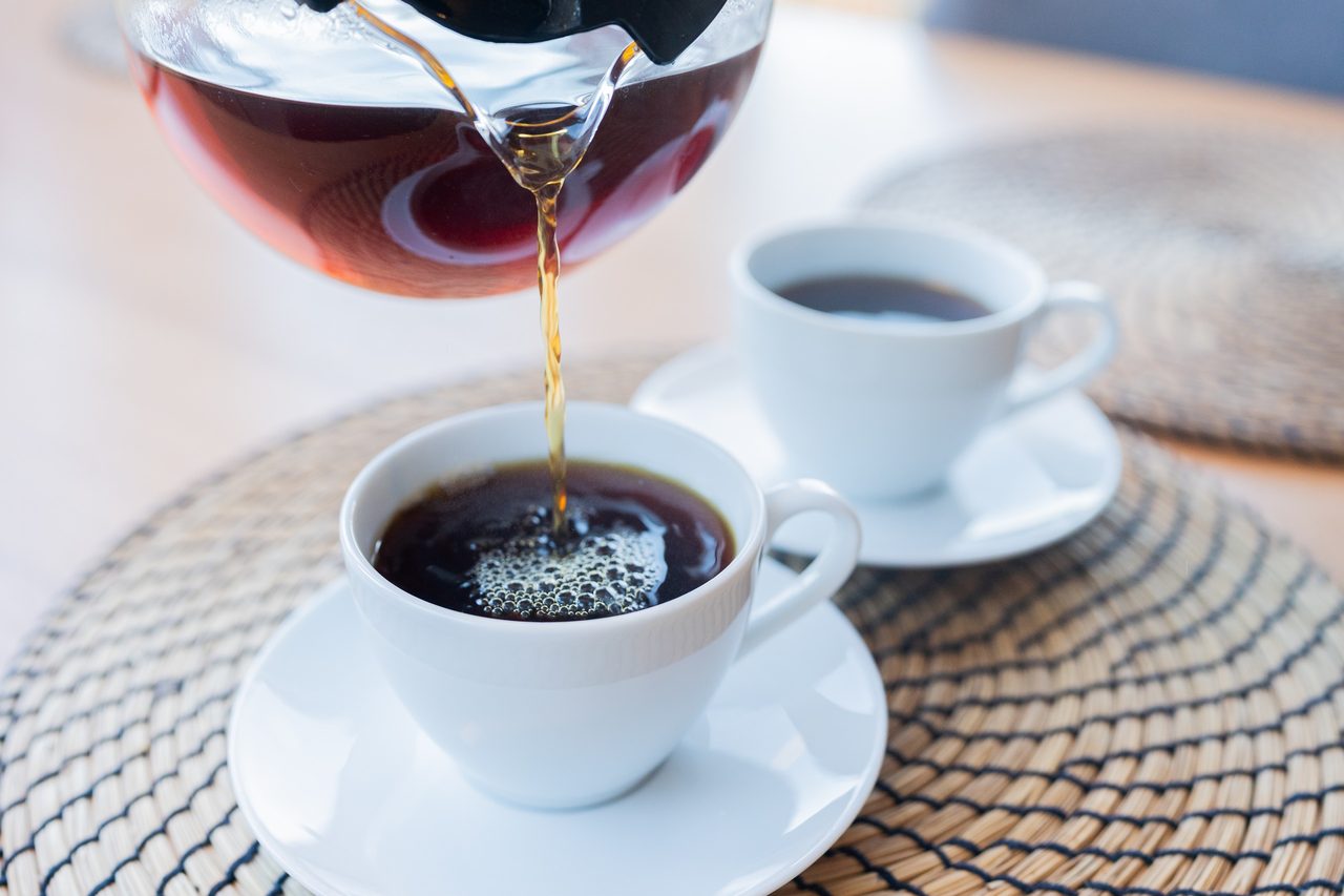 Kaffee wird aus einer Glaskanne in eine weiße Tasse gegossen
