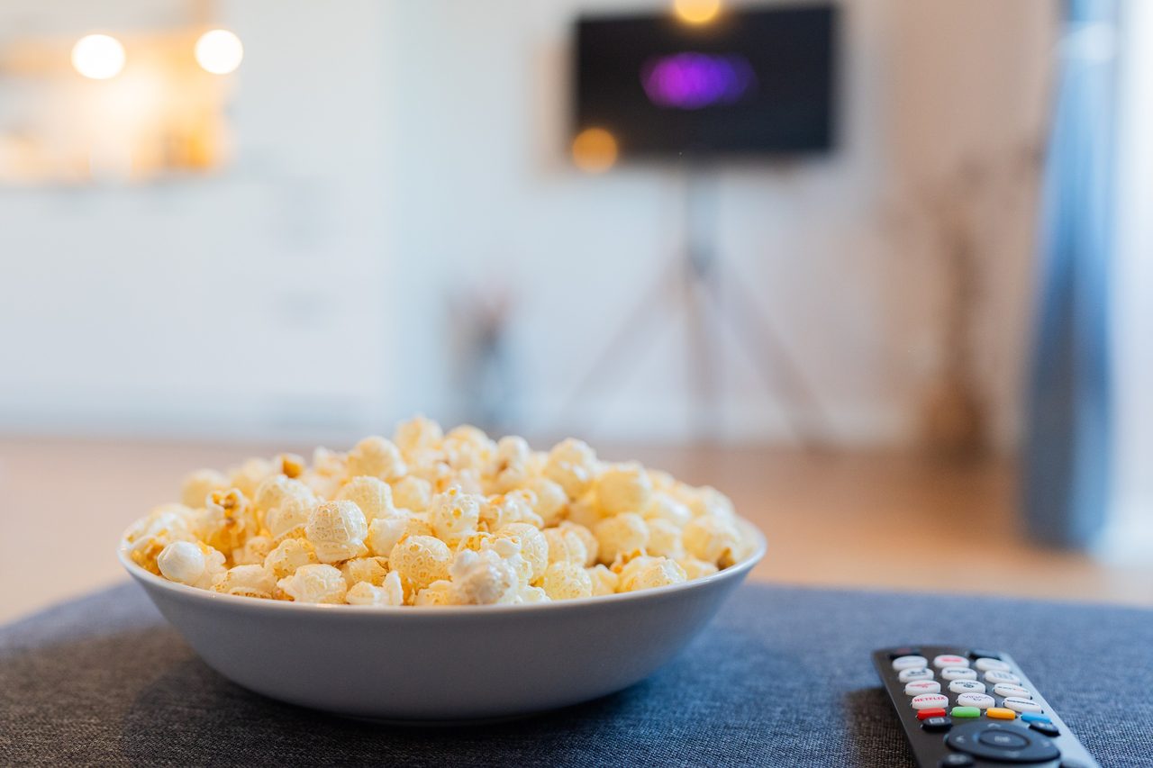 Schüssel mit Popcorn und Fernbedienung vor einem Fernseher