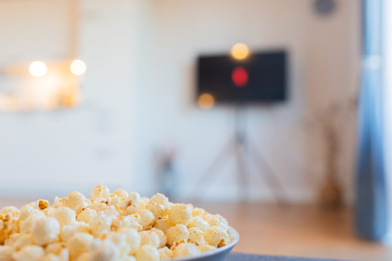 Schüssel mit Popcorn vor einem Fernseher im Hintergrund