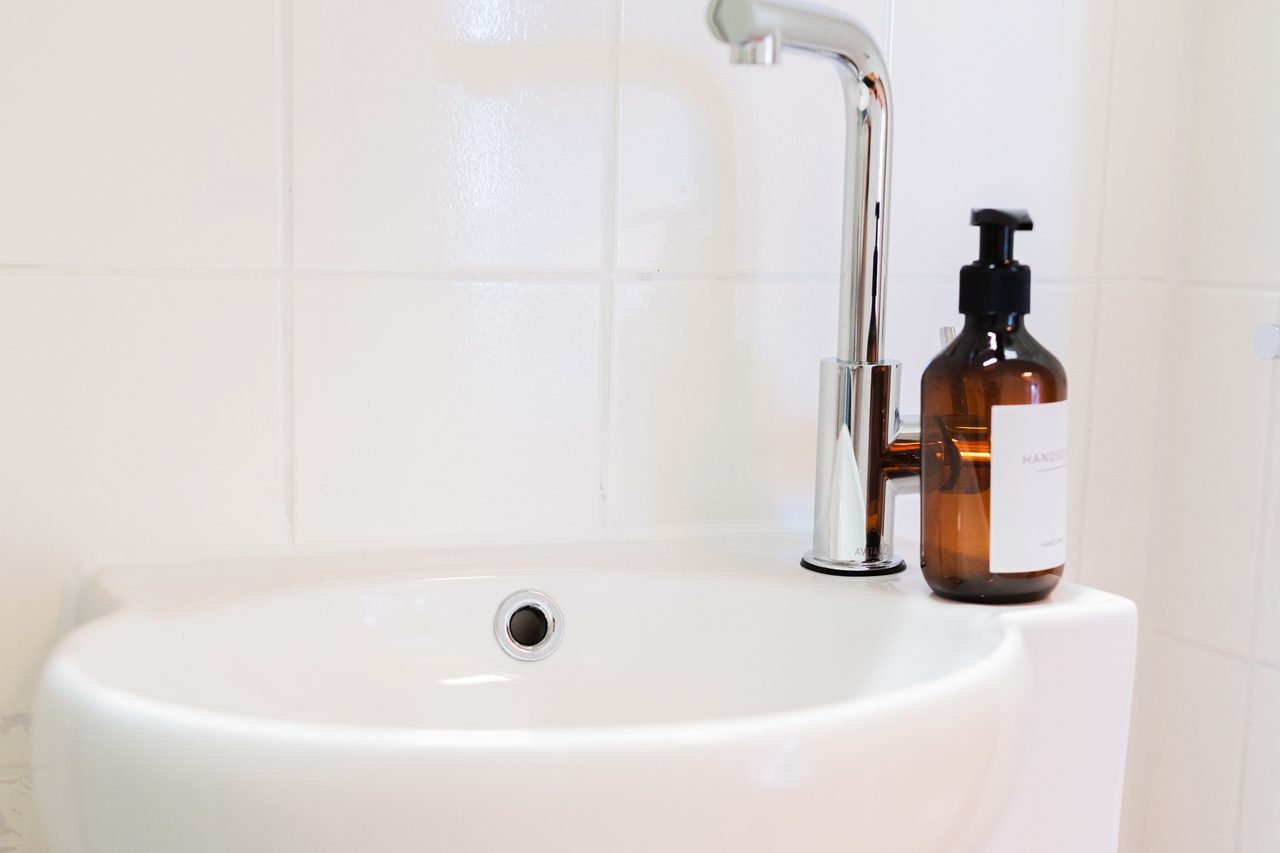 Kleines Waschbecken mit Armatur und brauner Seifenflasche