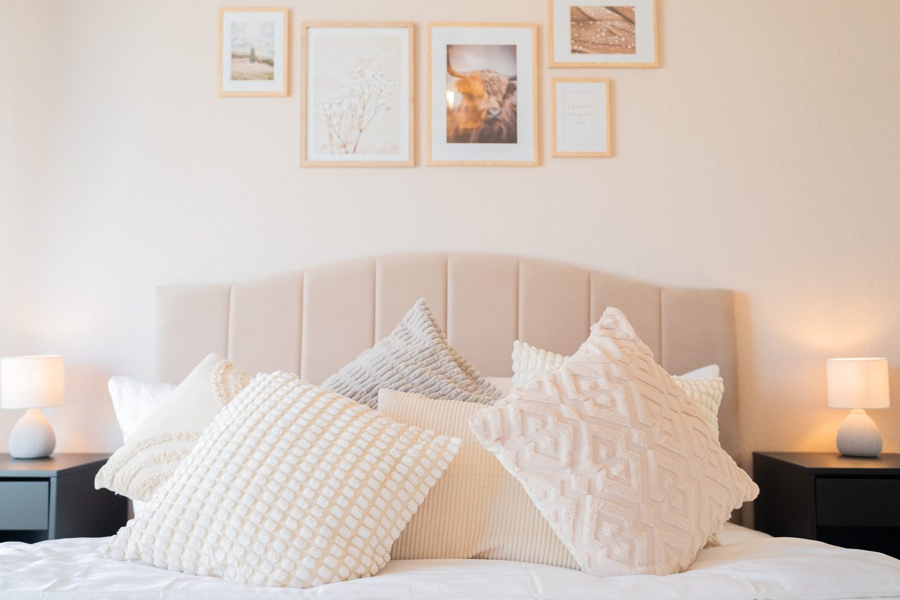 Doppelbett mit Polsterkopfteil, Kissen, Nachttischlampen und Wandbildern