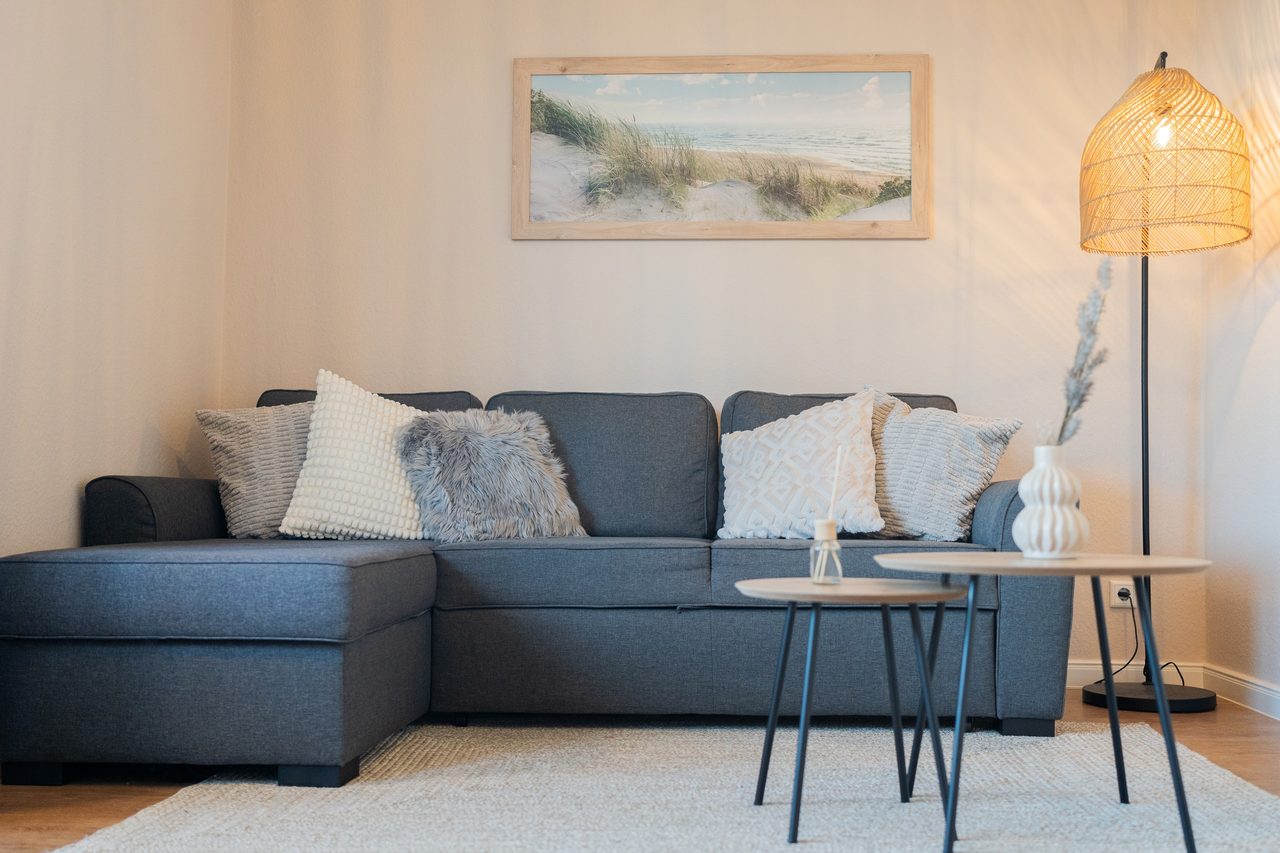 Wohnzimmer mit blauem Ecksofa, Beistelltischen und Stehlampe aus Rattan