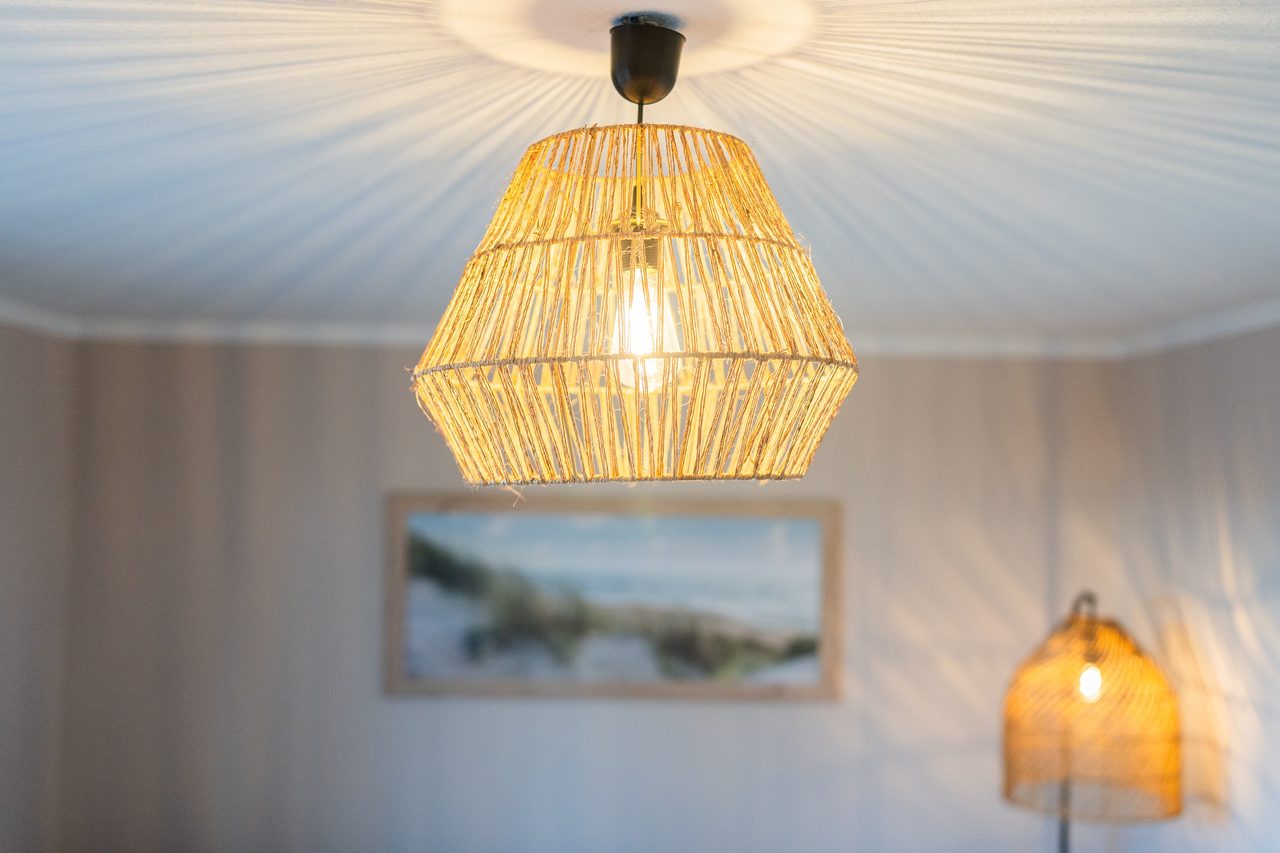 Pendelleuchte aus Rattan, Dünenbild und Stehlampe im Hintergrund
