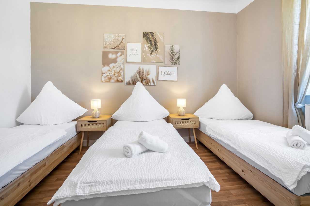 Schlafzimmer mit drei Einzelbetten, Nachttischlampen und Bildern an der Wand