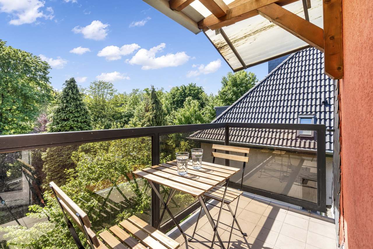 Balkon mit Klapptisch, Holzstühlen und Blick auf Bäume und Dach