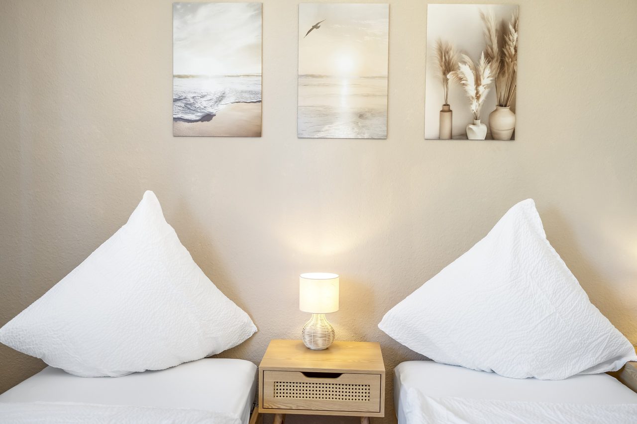 Schlafzimmer mit zwei Betten, Nachttischlampe und drei Wandbildern