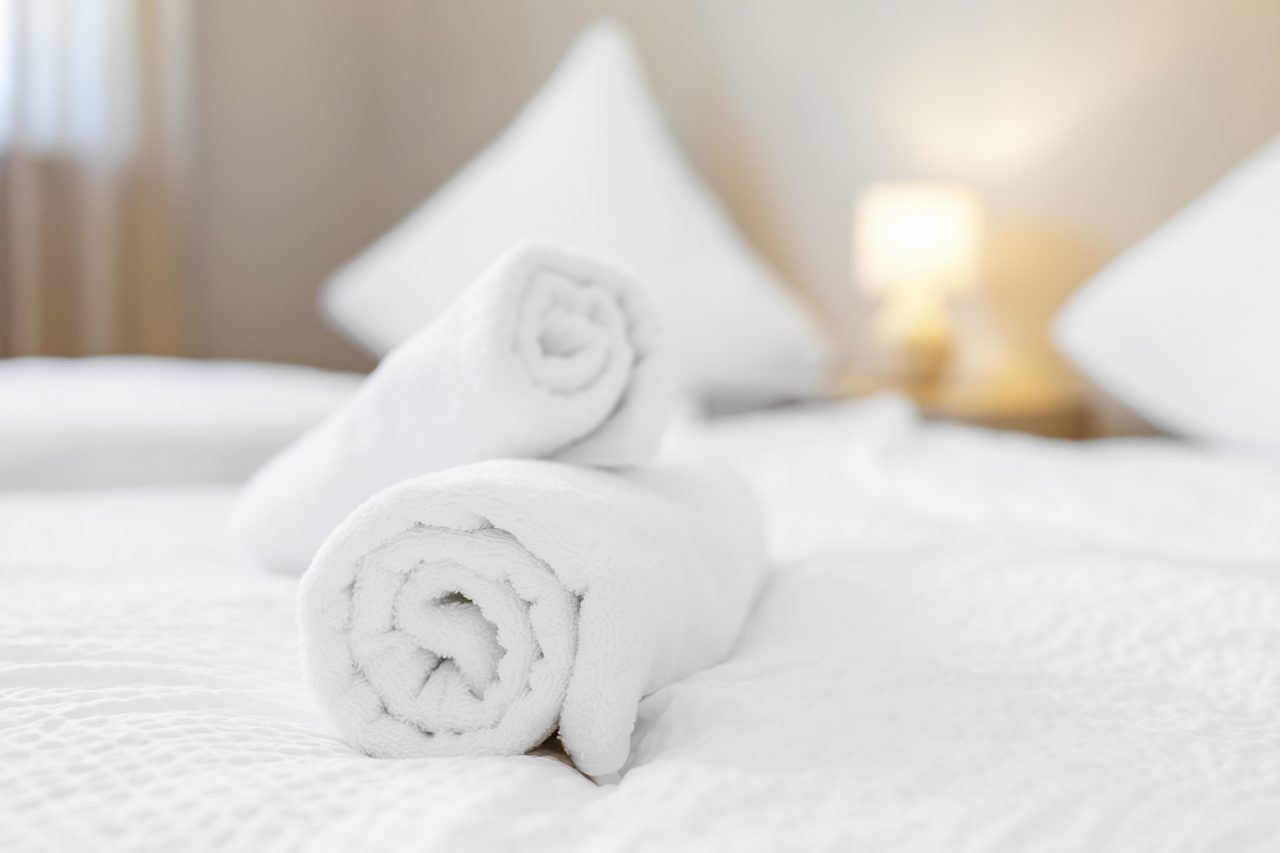 Gerollte weiße Handtücher auf einem Bett mit weißer Bettwäsche