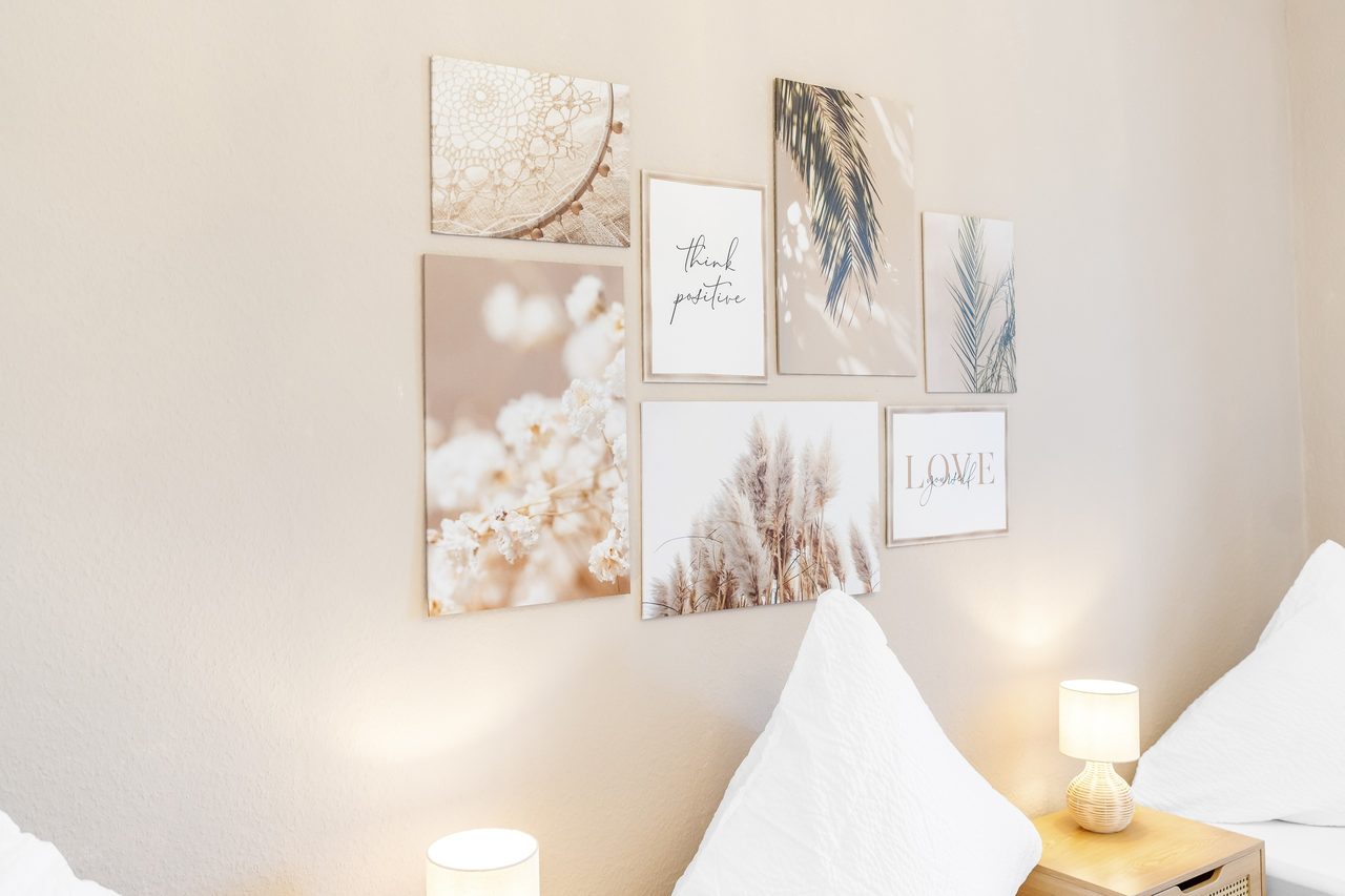 Bildercollage an beiger Wand über einem Bett mit Nachttischlampe