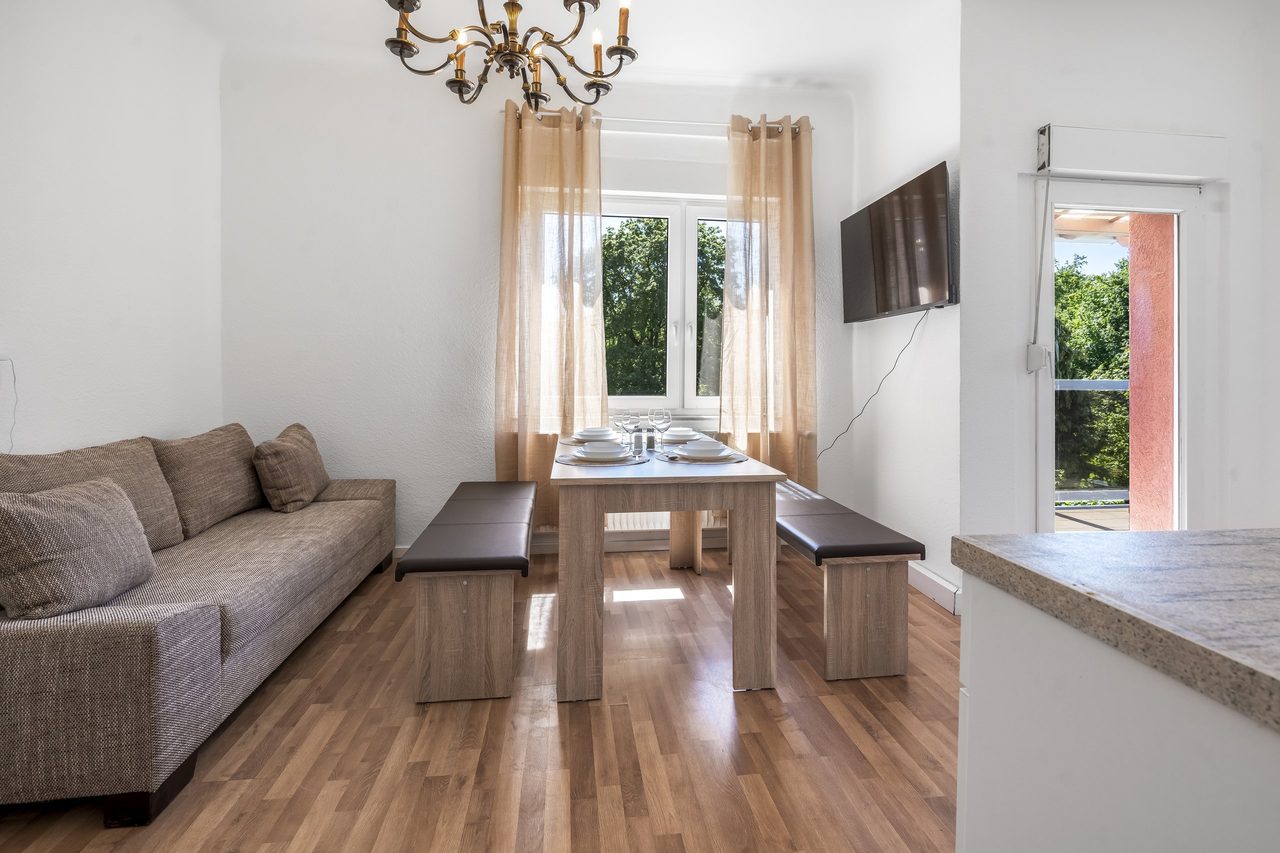 Wohnzimmer mit Sofa, Esstisch mit Bänken und Kronleuchter