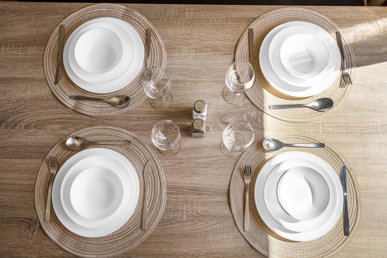 Holztisch von oben mit vier Gedecken, Gläsern und Besteck