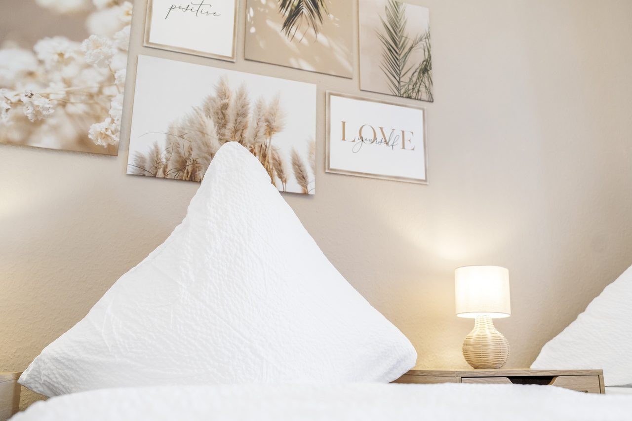 Weißes Kissen auf einem Bett mit Nachttischlampe und Wandbildern