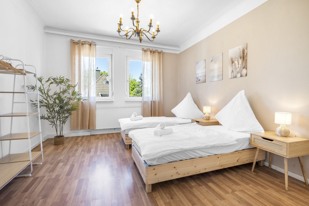 Schlafzimmer mit zwei Einzelbetten, Kronleuchter und zwei Fenstern