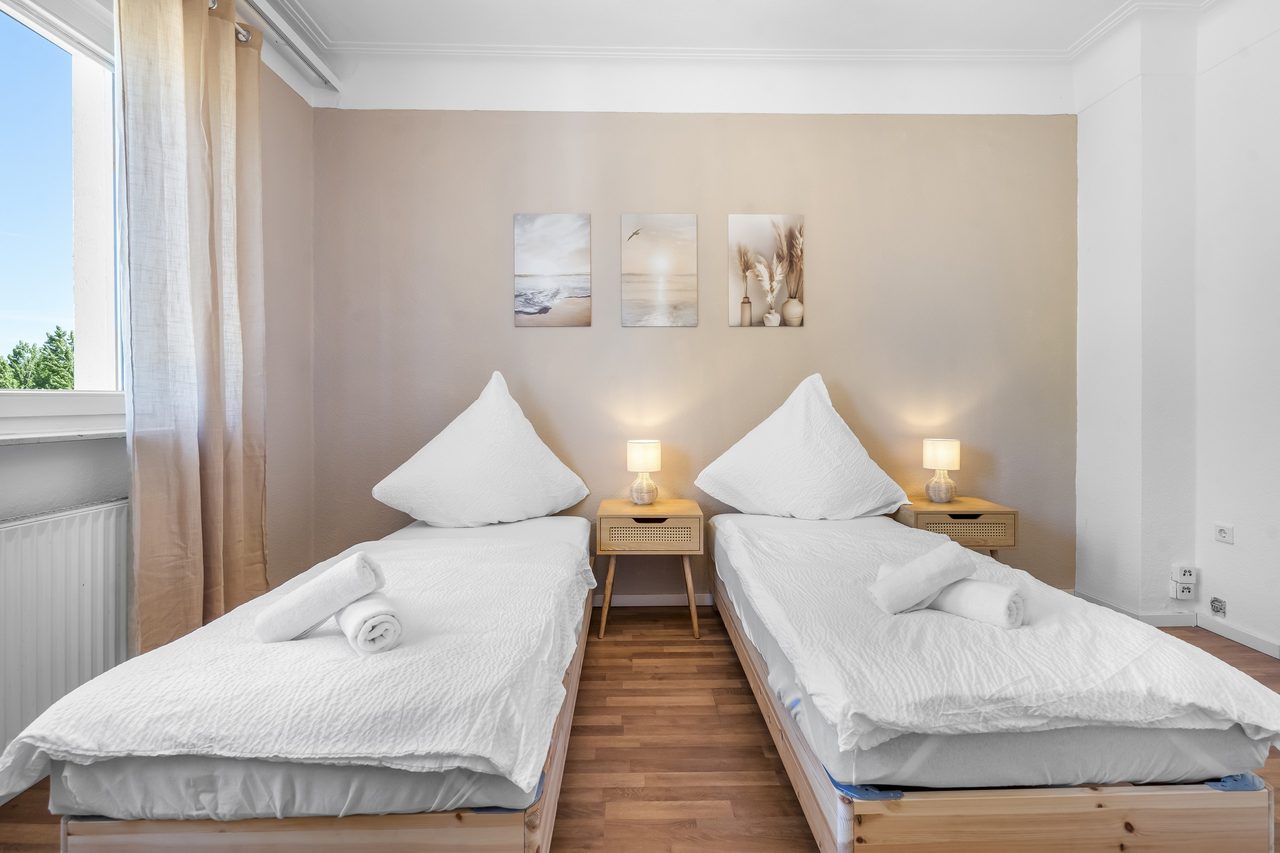 Schlafzimmer mit zwei Einzelbetten, gerollten Handtüchern und drei Wandbildern