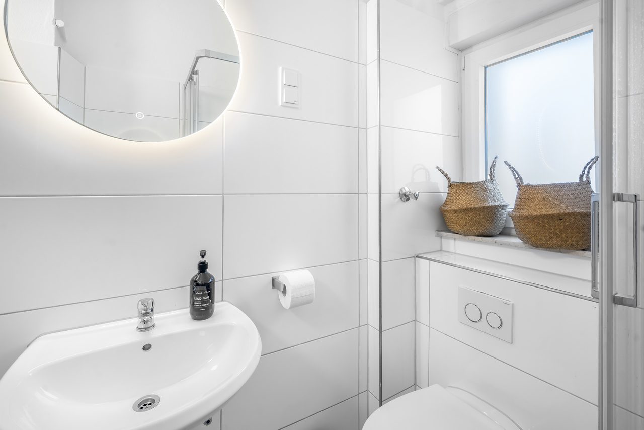 Badezimmer mit Waschbecken, rundem Spiegel und Körben auf dem Fensterbrett