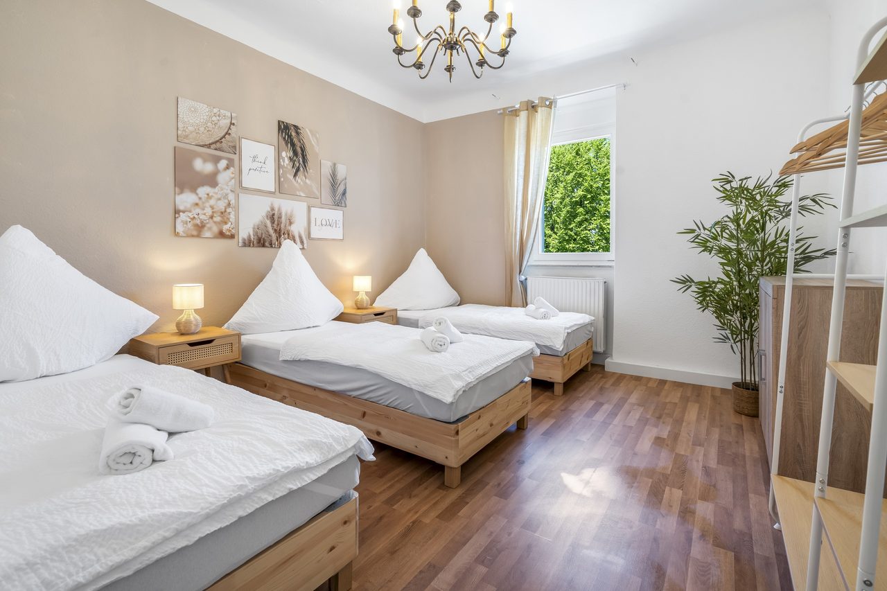 Schlafzimmer mit drei Einzelbetten, Kronleuchter und Zimmerpflanze
