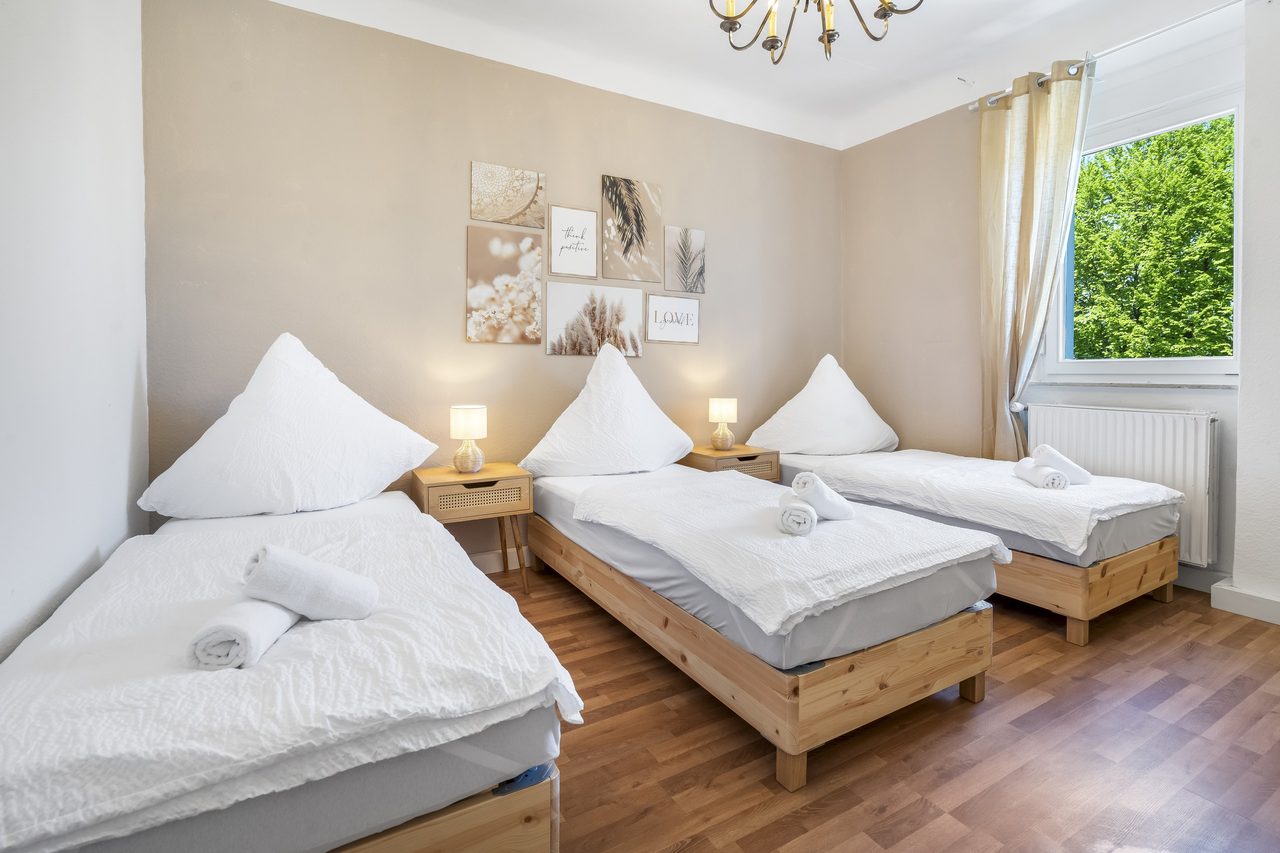 Schlafzimmer mit drei Einzelbetten, Nachttischlampen und Fenster