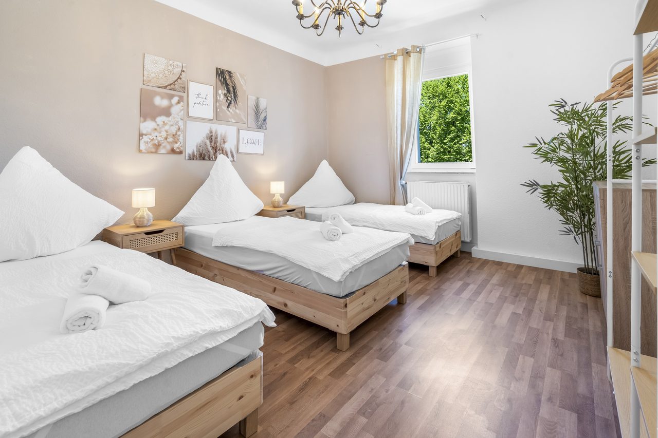 Schlafzimmer mit drei Einzelbetten, Bildercollage und Zimmerpflanze