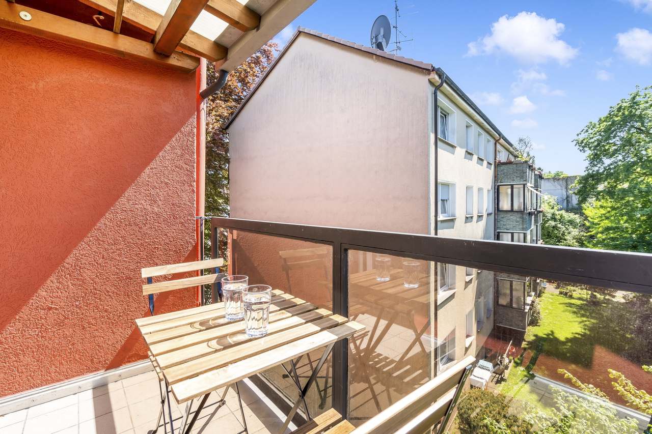 Balkon mit Holztisch und Blick auf Nachbarhäuser und Bäume